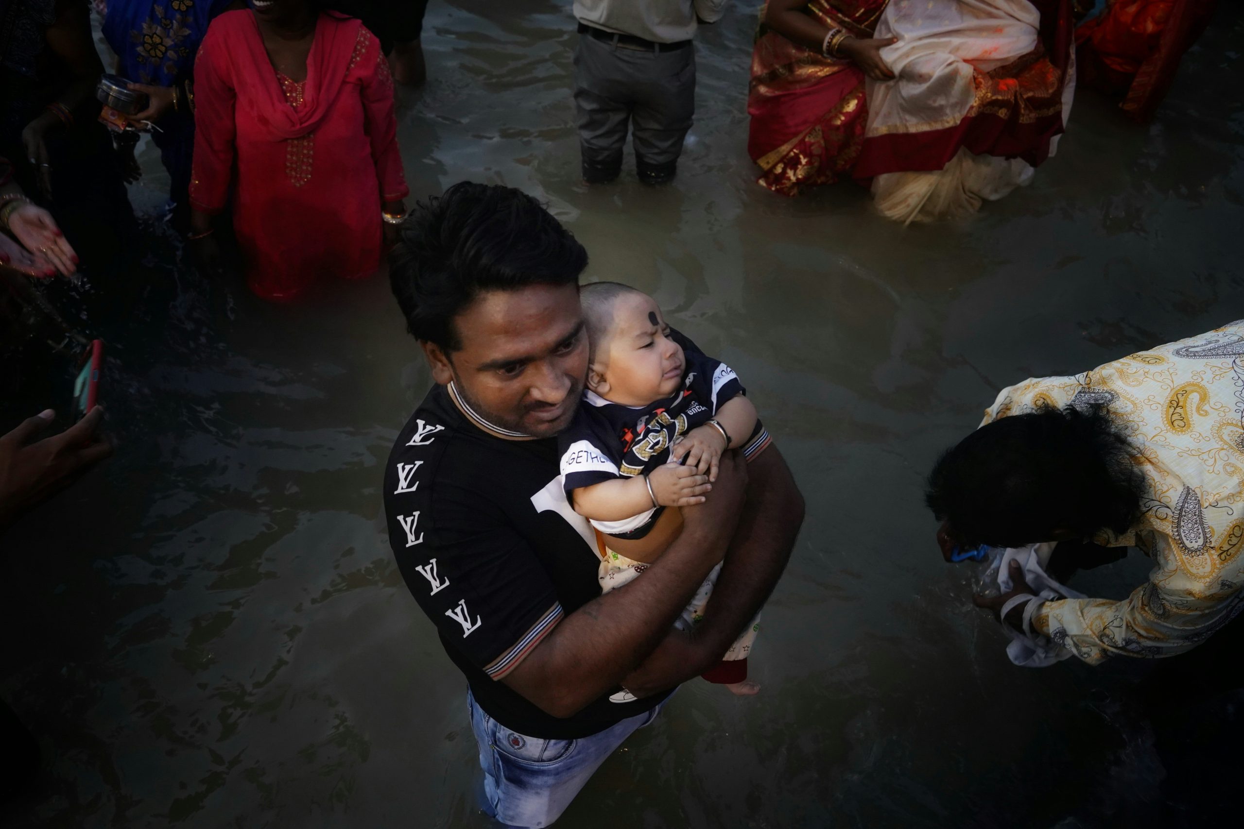 A man carries a baby while wading through floodwater alongside other people